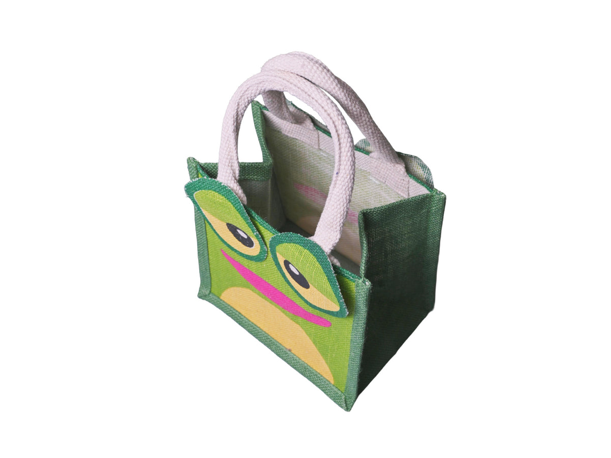 A green jute tote bag featuring a cartoon frog face design with large round eyes, yellow accents, and a pink mouth, complete with cotton cord handles, facing 45 degrees to the left from an angled aerial view, shown on a plain white background.