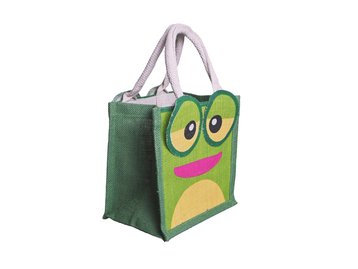 A green jute tote bag featuring a cartoon frog face design with large round eyes, yellow accents, and a pink mouth, complete with cotton cord handles, facing 45 degrees to the right, shown on a plain white background.
