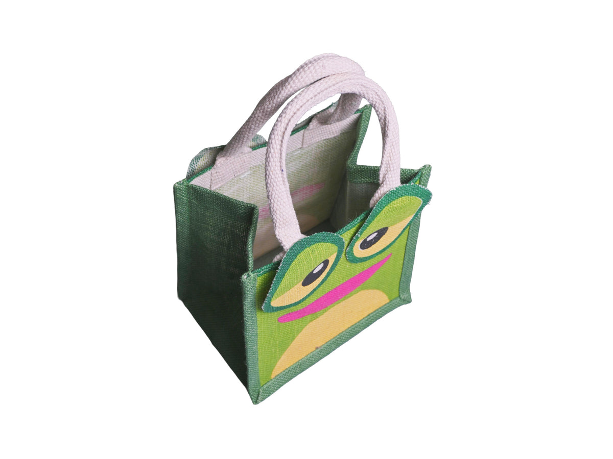 A green jute tote bag featuring a cartoon frog face design with large round eyes, yellow accents, and a pink mouth, complete with cotton cord handles, facing 45 degrees to the right from an angled aerial view, shown on a plain white background.